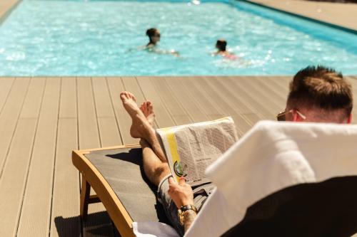 a man sitting in a chair reading a book next to a swimming pool at Novotel Nancy in Nancy