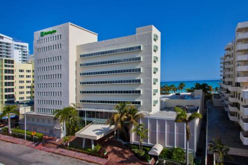 a tall white building with palm trees in front of the ocean at Holiday Inn Miami Beach-Oceanfront by IHG in Miami Beach