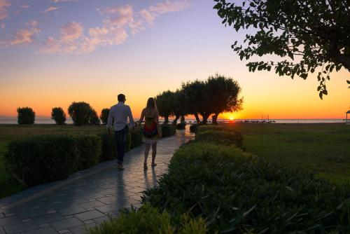 a man and a woman walking down a sidewalk at sunset at Atrium Palace Thalasso Spa Resort And Villas in Kalathos