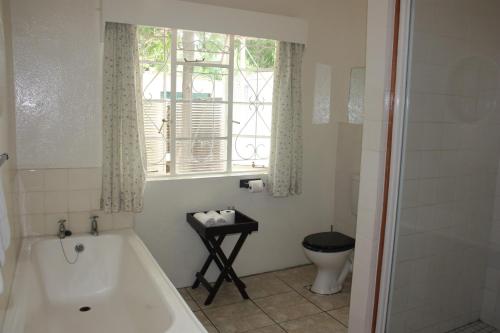 a bathroom with a tub and a toilet and a window at Karoopark Guest House in Graaff-Reinet