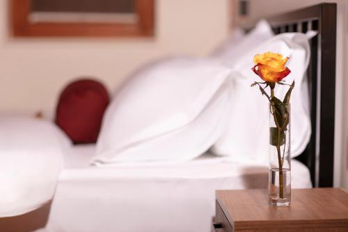 a vase with a rose on a table in a bedroom at Grand Boutique Hotel in Pristina
