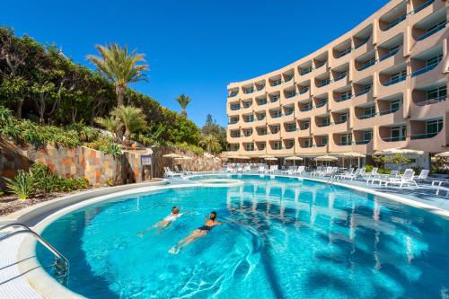 two people swimming in a swimming pool next to a hotel at MUR Aparthotel Buenos Aires Gran Canaria in Playa del Ingles