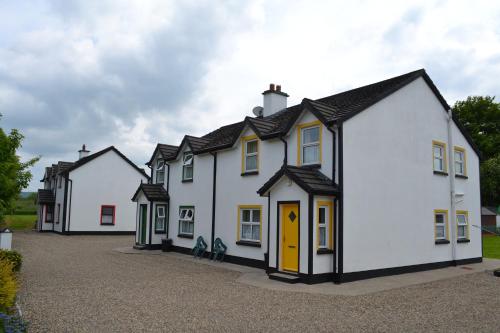 a row of white houses with a yellow door at Riverbank Cottages in Scarriff