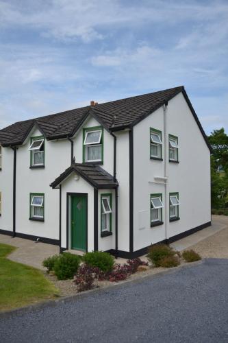 a white house with a green door on a street at Riverbank Cottages in Scarriff
