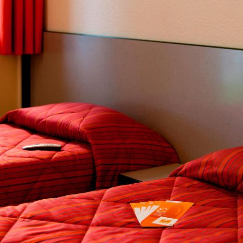 two beds in a hotel room with red comforter at Premiere Classe Gueret in Guéret