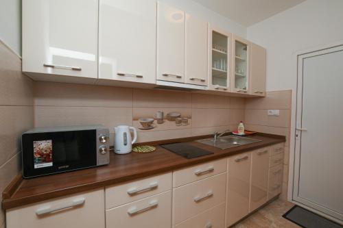 La cuisine est équipée de placards blancs et d'un four micro-ondes. dans l'établissement Apartman Netra, à Kladovo