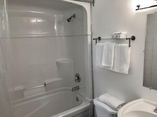 a white bathroom with a tub and a toilet and a sink at Pines Motel in Sicamous