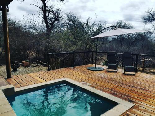 a pool on a wooden deck with two chairs and an umbrella at Bush and Gables House in Marloth Park