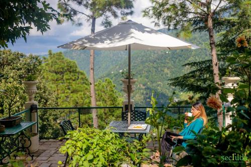 a woman sitting at a table under an umbrella at Seclude Ramgarh Taradale in Rāmgarh