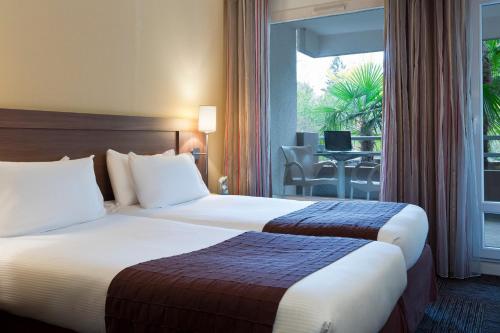 a hotel room with two beds and a balcony at Résidence la Réserve Genève Ferney Voltaire in Ferney-Voltaire
