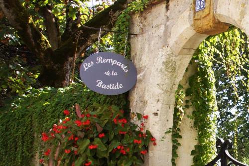 un panneau sur le côté d'un bâtiment avec des fleurs dans l'établissement Les remparts de la Bastide, à Castillonnès
