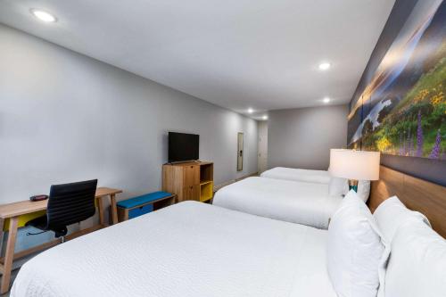 a hotel room with two beds and a desk and a tv at Days Inn & Suites by Wyndham Downtown/University of Houston in Houston