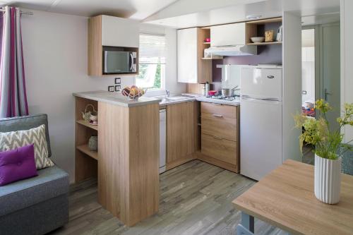 cocina con armarios de madera y nevera blanca en Mobil Home XXL 4 chambres - Camping Le Domaine de Bréhadour, en Guérande