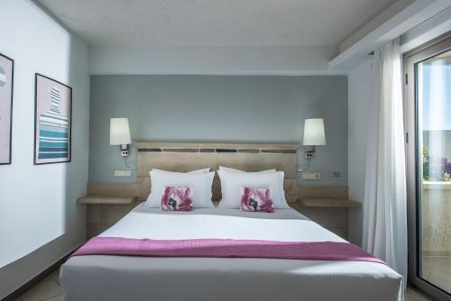 a bedroom with a large white bed with pink pillows at Skajado Holiday Apartments in Stalida