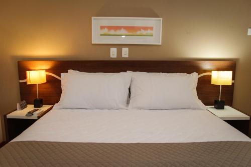 a bedroom with a bed with white pillows and two lamps at Bristol Centro Civico Curitiba in Curitiba