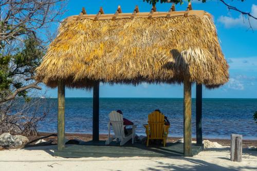 two people sitting in chairs under a straw hut on the beach at Kawama Yacht Club Apartment in Key Largo