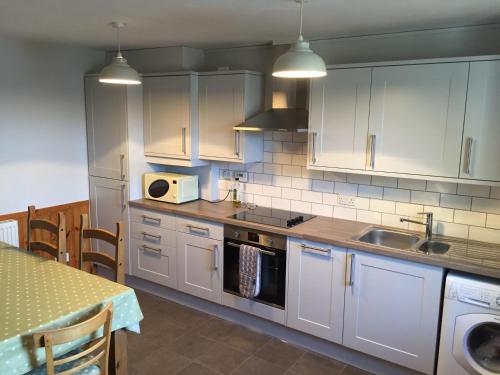 a kitchen with white cabinets and a sink and a table at George's House - 1 Leacklee in Manish