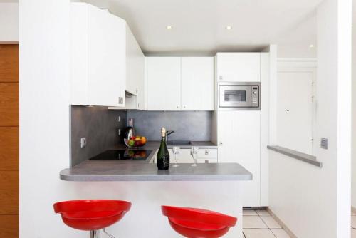 une cuisine blanche avec des tabourets rouges et un comptoir dans l'établissement Résidence Saint Rémy 2, à Cannes