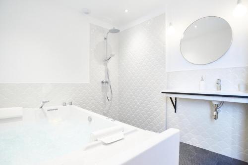 uma casa de banho branca com uma banheira e um espelho. em Maison 1634 - Centre historique, parking, petit-dejeuner compris, climatisation, piscine em Pézenas