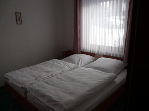 een bed met witte lakens voor een raam bij Appartementhaus Looss in Altenau