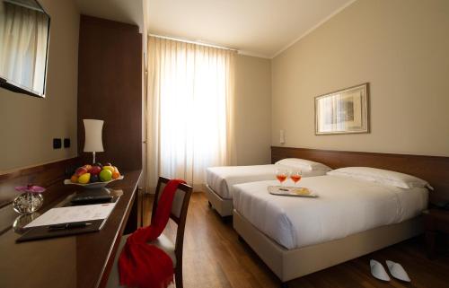 a hotel room with two beds and a table with a bowl of fruit at Hotel Fenice in Milan