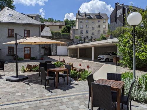 un patio con mesas, sillas y una sombrilla en Logis Regina, en La Bourboule
