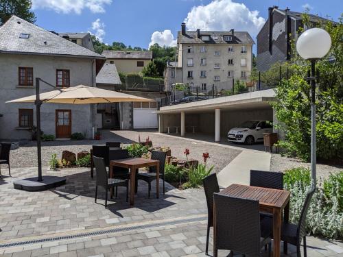 eine Terrasse mit Tischen, Stühlen und einem Sonnenschirm in der Unterkunft Logis Regina in La Bourboule