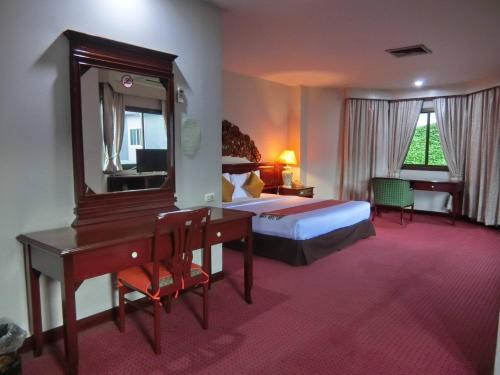 a hotel room with a bed and a desk and a mirror at Inn Come Hotel Chiang Rai in Chiang Rai