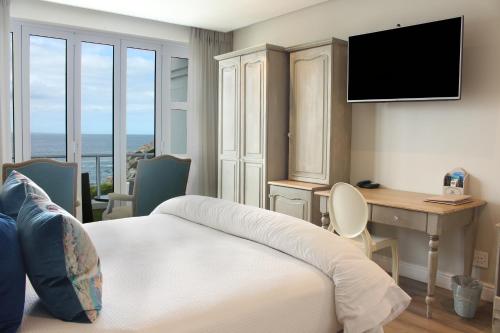 ヘルマナスにあるHermanus Boutique Guest Houseのベッド、デスク、テレビが備わるホテルルームです。