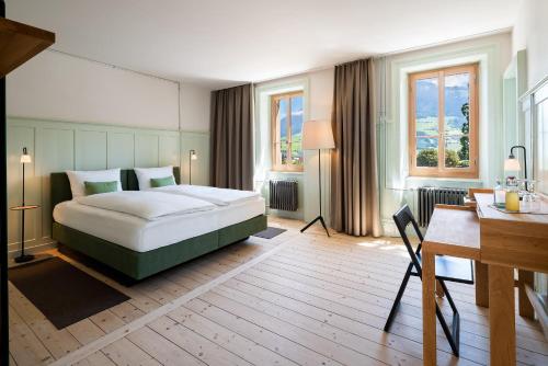 a bedroom with a bed and a desk and windows at Culinarium Alpinum in Stans