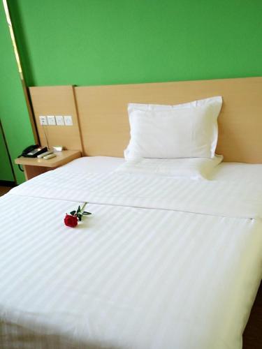 a red rose on a white bed with a green wall at 7Days Inn Huanggang Luotianhedong Street Dabieshan Night Supper Plaza in Luotian