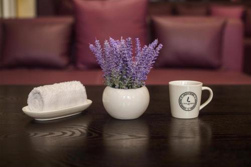 a white vase with purple flowers in it next to a coffee mug at Lavande Hotel Rizhao Rong'an Square Wanda Movie Theater Branch in Rizhao
