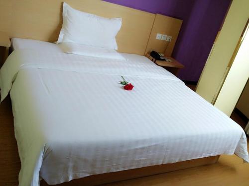 Una cama blanca con una rosa roja. en 7Days Inn Huanggang Luotianhedong Street Dabieshan Night Supper Plaza, en Luotian