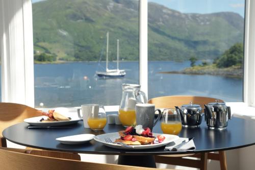 a table with food and orange juice and a view of the water at The Isles of Glencoe Hotel in Glencoe