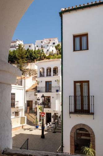 a white building with an arch next to a street at Olive & Ivy Guesthouse in Canillas de Aceituno