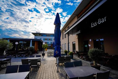 un patio con tavoli, sedie e ombrellone blu di Hotel Viktorosa a Hofgeismar