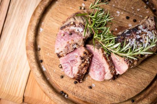 a piece of meat on a wooden plate with rosemary at Hotel Martellerhof in Martello
