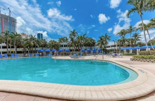 a large swimming pool with palm trees and blue umbrellas at Beautiful Apartment Steps Away from the Beach in Miami Beach