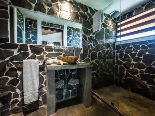 uma casa de banho com uma parede de pedra, um lavatório e um espelho. em Hotel Peace & Lodge em Sámara