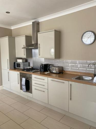 a kitchen with white cabinets and a clock on the wall at Harlow Coach House in Harrogate