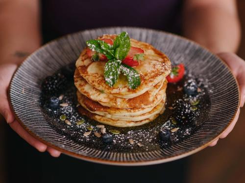 a person holding a plate with a stack of pancakes at The Grand Hotel in Swansea