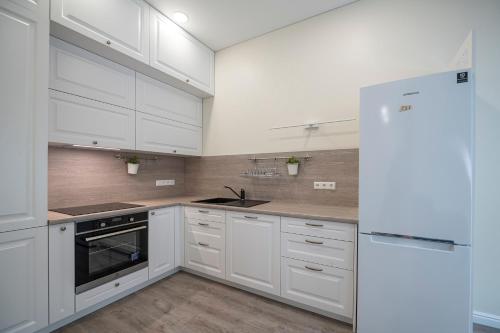 een witte keuken met witte kasten en een koelkast bij Botanical garden apartment in Kaunas