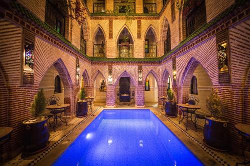 an indoor swimming pool in a building with tables and chairs at Riad Challa Hotel & Spa in Marrakesh
