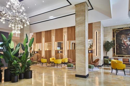 a lobby with yellow chairs and a chandelier at Silken Reino de Aragón in Zaragoza