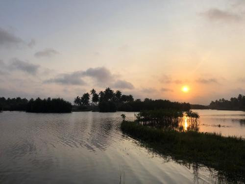 a sunset on a lake with the sun setting at Natura luxury red house in Ouidah