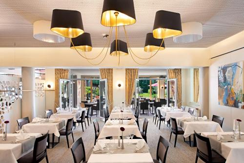 バート・シェーンボルンにあるホテル ヴィラ メディチの白いテーブルと椅子、シャンデリアのあるレストラン