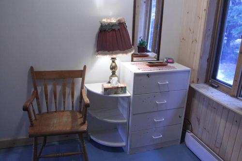 a dresser with a lamp and a chair in a room at La maison du capitaine est à vous! in Tadoussac