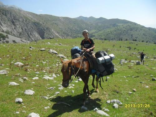 a man riding a donkey on a grass field at Panorama in Arslanbob