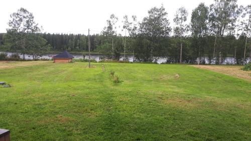 a large grass field with a gazebo and a lake at Savutaival in Pello