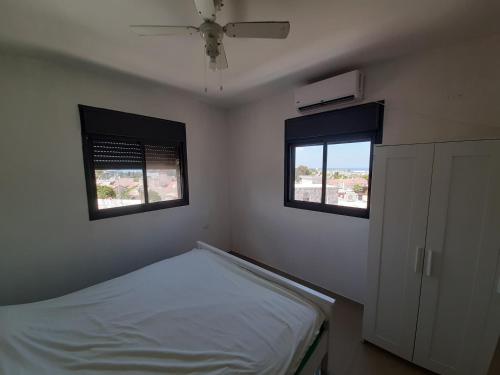 a small bedroom with a bed and two windows at Family apart in Nahariyya